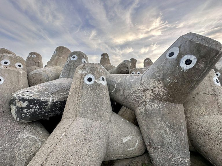Betonklötze mit Augen stehen in einer Gruppe unter einem bewölkten Himmel.